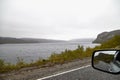 View from the car window of sad, harsh, dramatic landscape with a lake, river or fjord, a rock in the distance on the horizon and Royalty Free Stock Photo