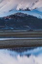 A view of Castelluccio di Norcia in front of a big snowed mountaind and reflected in a lake in the valley