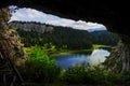 view from a cave to a wonderful blue mountain lake with trees hills and meadow Royalty Free Stock Photo