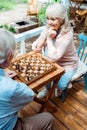 View of cheerful retired woman playing chess with senior husband