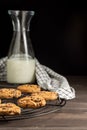 View of chocolate cookies on rack, bottle with milk and cloth, selective focus, on wooden table, and black background, vertical, Royalty Free Stock Photo