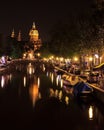 View of a church and a canal in Amsterdam, Netherlands at night. The Basilica of Saint Nicholas Sint-Nicolaasbasiliek with the r Royalty Free Stock Photo