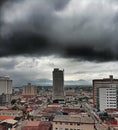 view of the city with a building under construction, mountains in the background, cloudy sky with heavy rain clouds Royalty Free Stock Photo