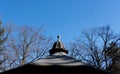 View of clear blue winter sky with decorative tiled pavilion roof and bare tree tops - with copy space in the sky