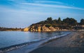 View of the coast beach in the background a rocky ledge covered with green trees and bushes.