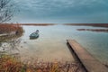 view from the coast of the lake to a beautiful water landscape with a boat, wooden pier and coastal reeds in the light of autumnal Royalty Free Stock Photo