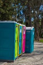 View of colored portable bathroom cabins surrounded by greenery in a park