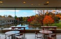 View of colorful maple trees by a lake in the garden behind the floor-to-ceiling glass windows and wooden tables Royalty Free Stock Photo
