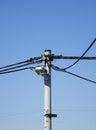 View of a column of power lines with telephone wires and a street lamp under a blue clear sky