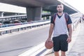 View with copy space of a forefront of a strong and attractive basketball player walking near a bridge with his ball and a Royalty Free Stock Photo