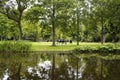 View of a couple sitting on a bench, people hanging out, trees, grass field and pond at Vondelpark