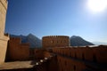 View of the crenelated walls of the fortress with the backdrop of sunny mountains, Oman