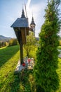 View on the cross in front of the Church of St. Volbenka in autumn colors against a blue sky, Slovenia, Europe.