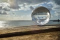 View Through A Crystal Ball On An Old Extended Wooden Bench Over The Sea With The Mudflats And The Sky With Clouds