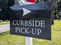 View of a curbside pickup sign in the grass outside a large business property during coronavirus