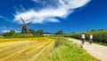 View on cycling path with cyclists couple in rural dutch limburg maas landscape with windmill Molen de grauwe beer against blue