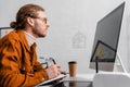 View of 3d artist looking at computer monitor and writing on notebook at table