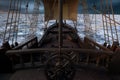 View of the deck from behind the ships wheel on an old pirate sailing ship in open sea with grey clouds. 3D rendering