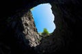 View from the deep cave through the shaft hole in the marble rock - a tree on the edge of the abyss and a bright sky Royalty Free Stock Photo