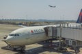 View of Delta aircraft connected to boarding bridge on front and another aircraft taking off on background. USA.