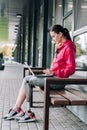 View of disabled sportswoman sitting on bench and using laptop on street