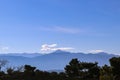 View of distant blue mountains of Peloponnese in Greece under blue sky with a few clouds and dark green trees in foreground Royalty Free Stock Photo