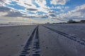 View down a deserted beach with truck tire tracks toward a long pier and a dramatic cloudscape and blue sky Royalty Free Stock Photo