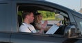 View of driving instructor holding checklist while in background female student steering and driving car. Driver courses Royalty Free Stock Photo