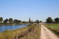 View on dutch cycling track along river Maas with village and church background in autumn on sunny day - Kessel, Netherlands