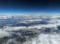 View of the earth from high altitude with dark blue sky and different types of white clouds with snow on a hilly landscape Royalty Free Stock Photo