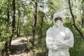 View of ecologist in protective costume and respirator with crossed arms in forest