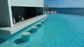 View on empty infinity pool with stone bar stools in water and counter, adriatic sea and blue summer sky background Royalty Free Stock Photo