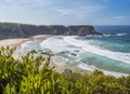 View of empty Praia dos Machados beach with ocean waves, cliffs and stones, wet golden sand and blurred green vegetation Royalty Free Stock Photo