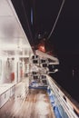 View of the empty ship deck at night with life boats and a lighthouse seen in the water