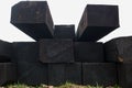 View of end parts of stacked rows of black tarred old rectangular railway sleepers lying on ground with grass, look of perspective