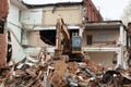 View of excavator on pile debris in front of a ruined old house