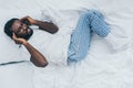 View of exhausted african american man suffering from headache while lying on white bedding Royalty Free Stock Photo