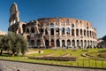 View of the exterior of the Colosseum in Rome with green meadow and ancient road in front on a spring day