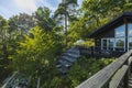 View of facade of typical wooden swedish house with wooden patio. Black walls and white windows with barbecue grill.