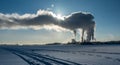 View of factory power plant in winter with steam rising into deep blue sky, sun shines behind steam