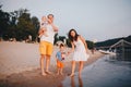 View Of Family With Two Toddler Children Outdoors By The River In Summer. Happy Young Family Have Fun On Beach At Sunset