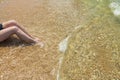 View of female sitting on sandbeach with legs in oncoming wave.