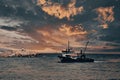 View of a fishing boat returning from the sea to land at sunset and a view of the small harbor, Royalty Free Stock Photo