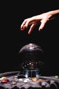 View of fortuneteller hand above crystal ball with fortune telling stones on black velvet cloth on black