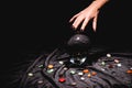 View of fortuneteller hand above crystal ball with fortune telling stones on black velvet cloth isolated on black