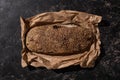 View of fresh baked loaf of whole grain bread with sesame in paper on stone black surface Royalty Free Stock Photo