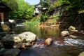 View of fresh river stream flow, stone bank and natural rock cascade with green trees and local buildings in Kurokawa onsen town Royalty Free Stock Photo