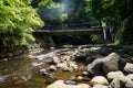 View of fresh river stream flow, stone bank and natural rock cascade with light glare around green trees and bridge in Kurokawa Royalty Free Stock Photo