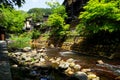 View of fresh river stream, stone bank and natural rock beach with green trees and local buildings in Kurokawa onsen town Royalty Free Stock Photo