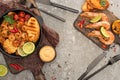 View of fried shrimps with grilled toasts, vegetables on boards near cutlery on grey concrete background